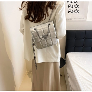 Silver quilted chain bag with heart-shaped metal lock worn by a model in a bedroom setting
