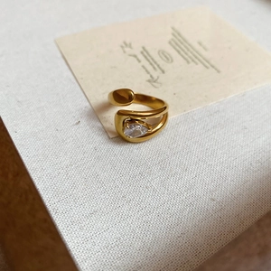 Detail of 18k gold plated open ring with a teardrop zircon on a textured background