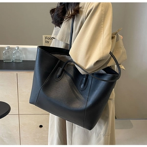Detail of minimalist black leather tote bag with slim shoulder strap worn by a model