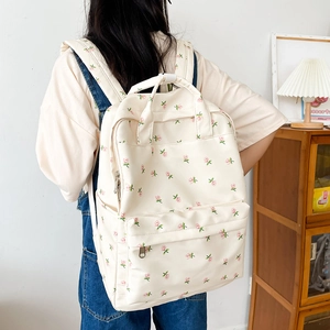 Detail of cream floral backpack with pink rose pattern worn by a model in a natural setting