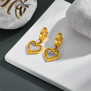 Close-up of golden heart earrings with white shell inlay on a white geometric block