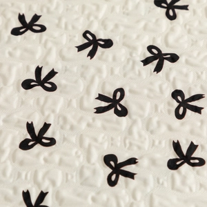 Close-up of cream textured fabric featuring a pattern of small black bows for laptop sleeve