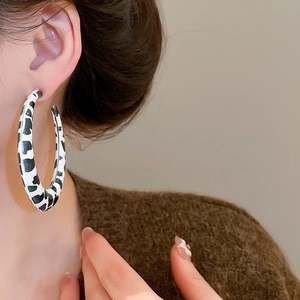 Close-up of a model wearing large circular cow print earrings with black and white spots