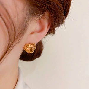 Close-up of golden mesh hollow heart earrings worn on ear showing intricate woven texture
