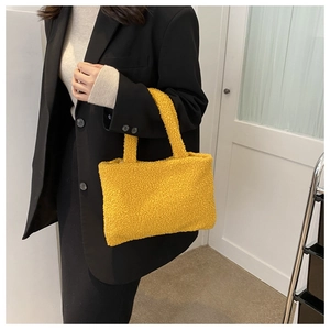 Close-up of a yellow plush handbag held by a model in a black blazer suit