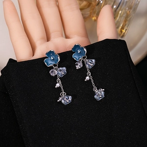 Detailed close-up of blue flower earrings with pearls on a black fabric background