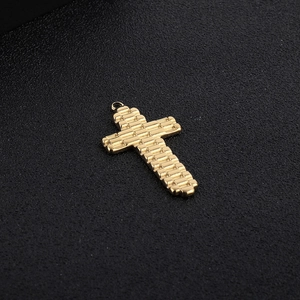 Gros plan du pendentif croix dorée avec une texture quadrillée et finition en métal