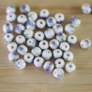 Detail of round white ceramic beads with blue-purple floral patterns for DIY jewelry