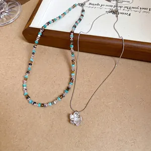 Floral stainless steel pendant necklace and colorful beaded strand on a wooden tray