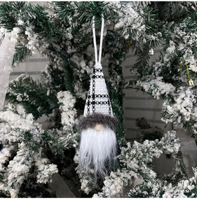 Close-up of Christmas gnome ornament with plaid hat hanging on snowy branch
