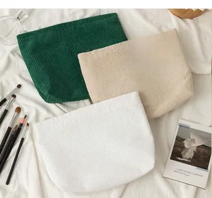 Detailed close-up of corduroy makeup bags in green, beige and white on soft cotton cloth