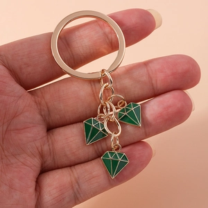 Detail of gold keychain with three green enamel diamond pendants held by a hand