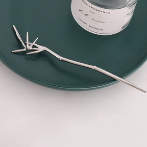 Detailed view of silver bamboo-shaped hair pin placed on a green plate with a candle