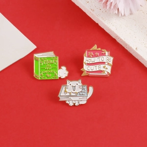 Detailed close-up of three colorful cat and book enamel pins on a vibrant red background