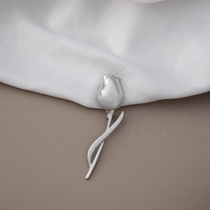 Close-up of silver tulip brooch with polished metal finish on soft textured background