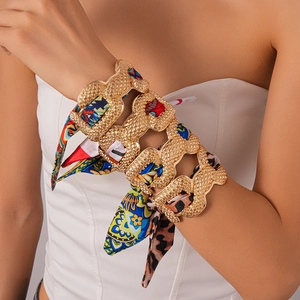 Macro detail of gold cuff bracelet with colorful silk fabric wrap and layered textures