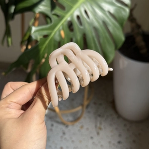 Elegant cream pumpkin hair claw clip held against a lush green leaf background