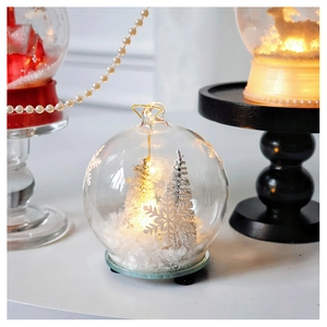 Close-up of glass Christmas ornament featuring a lit white tree and snowflake patterns