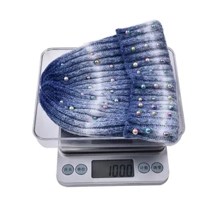 Berretto in maglia tie-dye blu e bianco con perle colorate del peso di 100 grammi su bilancia