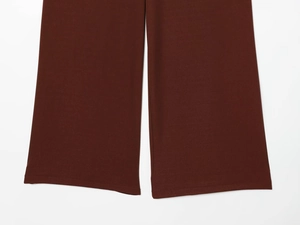 Detailed view of the wide-leg hem on dark brown trousers with matte fabric texture