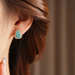 Close-up of golden gourd-shaped earring with blue gemstone and pavé white diamonds