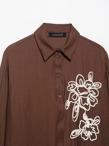 Detail of dark brown shirt featuring intricate white rope embroidery and textured fabric