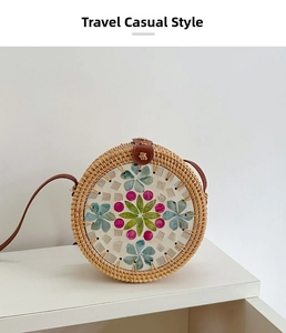 Close-up of handwoven round rattan bag featuring colorful floral mosaic and leather strap