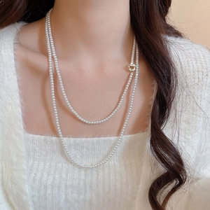Detail of multi-layer pearl necklace featuring a golden heart-shaped clasp on a model
