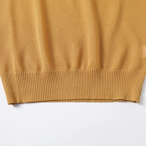 Close-up of ginger yellow knit polo shirt showing ribbed hem detail and high-quality texture