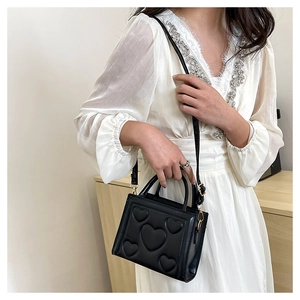 Détail d'un sac bandoulière noir avec motif cœur en relief et fine bandoulière chic