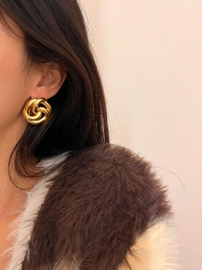 Macro detail of a 3D knotted gold-finished stud earring worn on model's ear