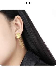 Detail of irregular textured gold earrings with long chain tassels on ear model