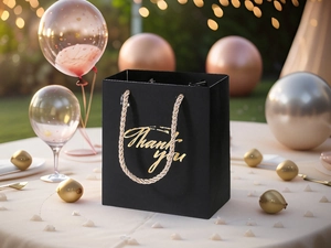 Elegant black thank you gift bag with gold handles on a festive party table background