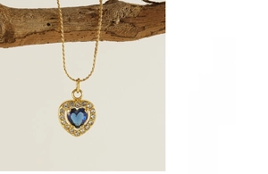 Detail of gold heart pendant with blue zircon surrounded by white stones on a branch
