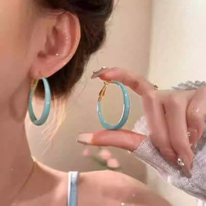 Close-up of a model wearing sky blue enamel round hoop earrings with golden metal clasps