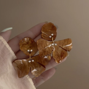 Macro shot of amber butterfly resin earrings with inlaid rhinestones on a beige background