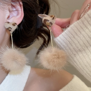 Close-up of leopard print heart and plush ball earrings worn by model for autumn style
