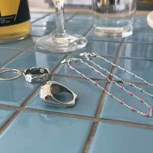 Detailed close-up of 925 sterling silver bead necklace and rings on blue tiles