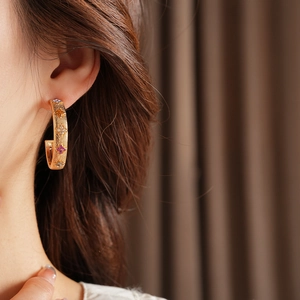Macro shot of gold-plated C-shaped earrings with colorful gemstone flowers on a model