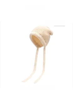 Detailed close-up of a beige knitted winter beanie with earflaps and hanging tie strings