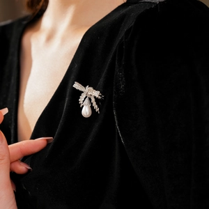 Détail d'une broche nœud argentée avec pendentif perle blanche sur du velours noir