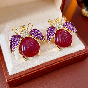 Close-up of vintage bee earrings with red shell bodies and purple enamel wings in a box