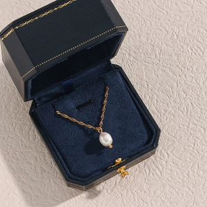 Dettaglio di un ciondolo con perla bianca e catena dorata in una scatola blu elegante