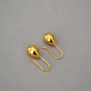 Close-up of polished gold teardrop earrings on a textured grey fabric background
