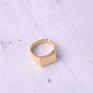 Detail van een vierkante zegelring met goudkleurige matte finish op wit houten decor