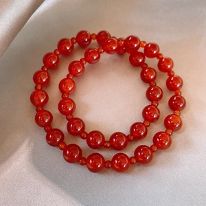 Detailed close-up of two red agate beaded bracelets on elegant silk fabric background