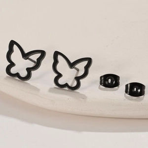 Detail of hollow butterfly earrings in black finish on a beige textured platform