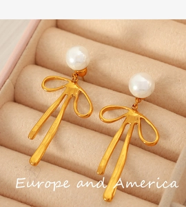 Detailed view of golden bow earrings with white pearls lying on a beige jewelry tray