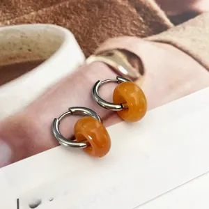 Close-up of silver earrings with orange resin hoops on a white display card