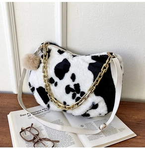 Detail of cow print plush tote bag with gold chain strap on an open book